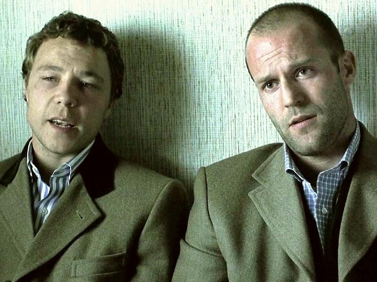Two men in suits leaning against a wall
