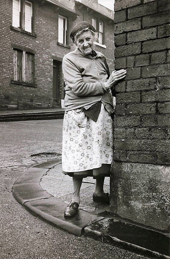 elderly woman leaning against brick wall
