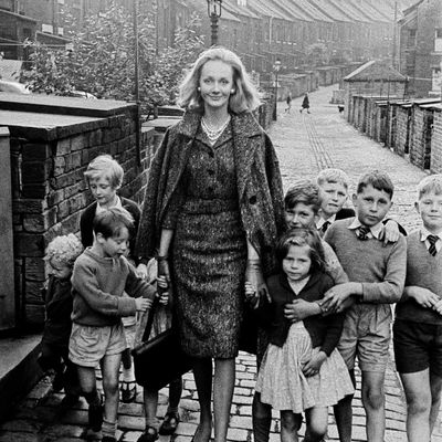 Woman Surrounded by Children woman children alleyway patterned dress coat