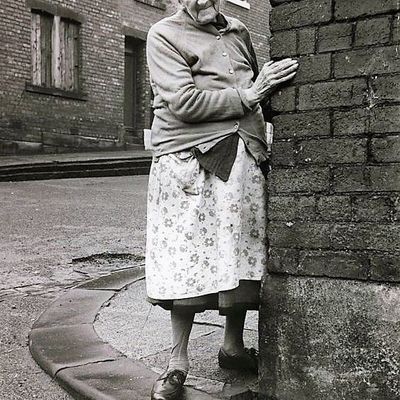 elderly woman leaning against brick wall