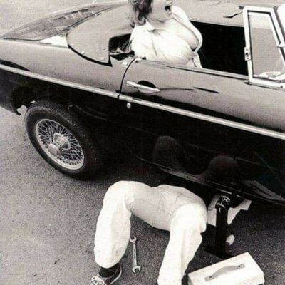 Woman in Fur Coat Inspecting Car Undercarriage
